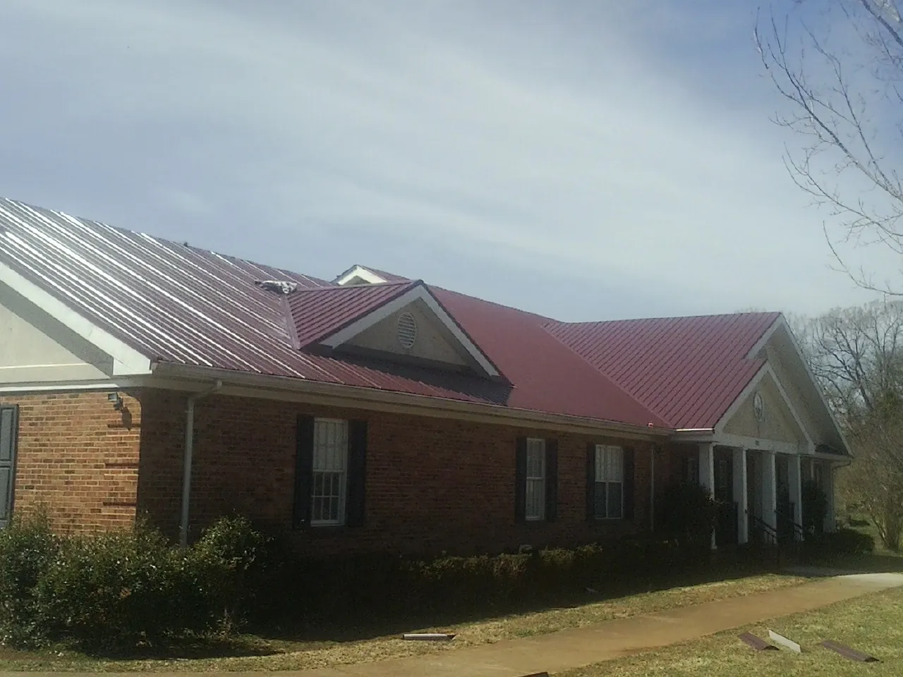 Red metal roof with gabled entries on a long brick building, from a Hail Damage Roof Repair job in Harwinton