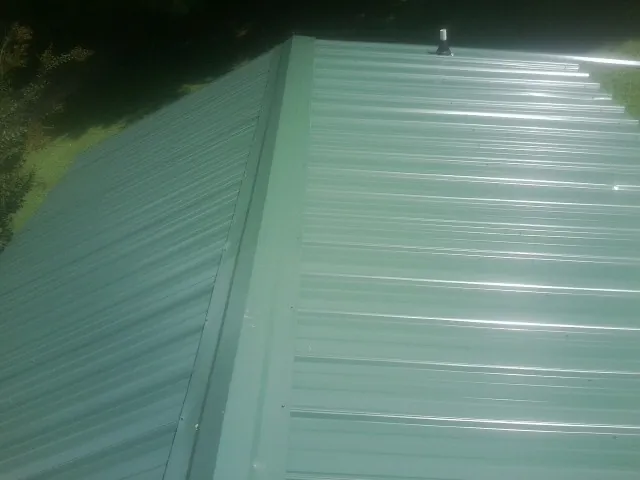 New green metal panels meeting at the ridge of a roof — Flat Roof Repair work by our crew in Harwinton