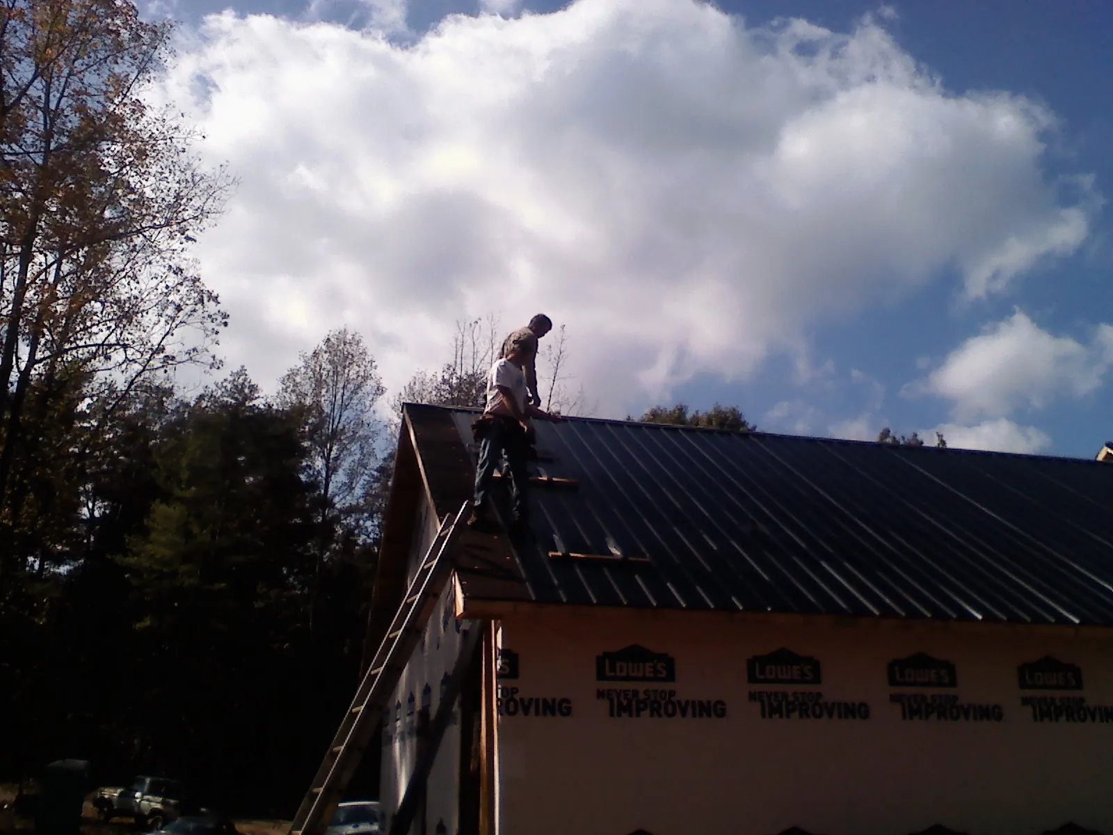 Roofer fastening dark metal panels high against a cloudy sky, from a Roof Inspection job in Harwinton