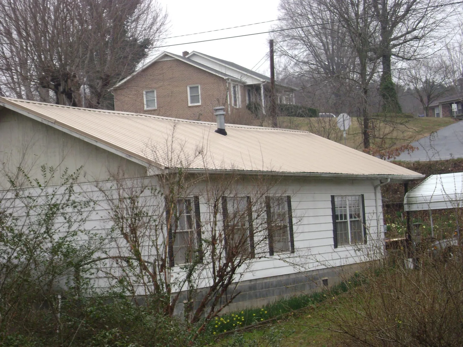 Tan metal roof on a white sided house set into a hillside — Commercial Roofing by Roofing Brothers in Harwinton