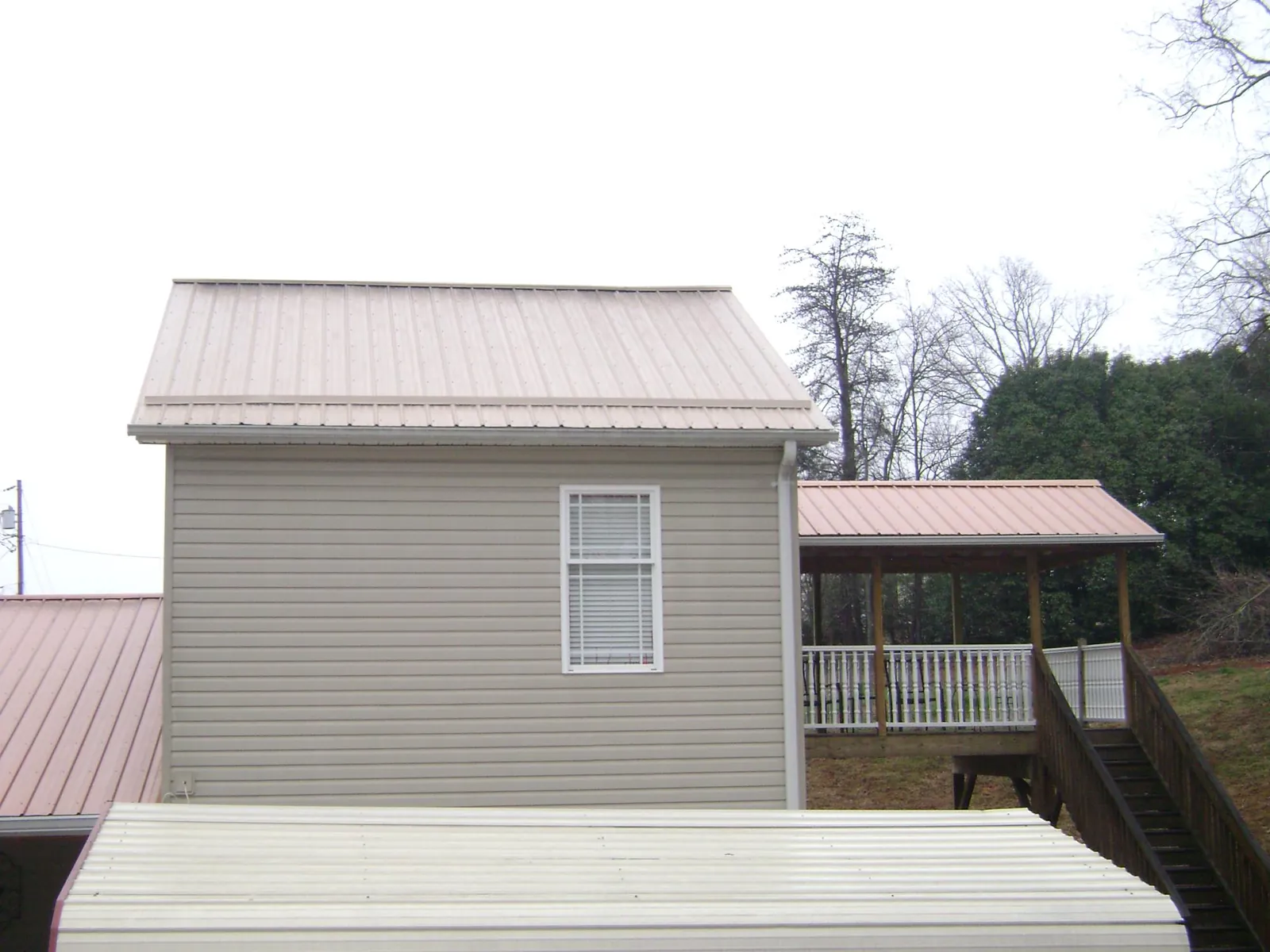 Tan metal roofs on a two story addition and attached porch, from a Roof Replacement job in Harwinton